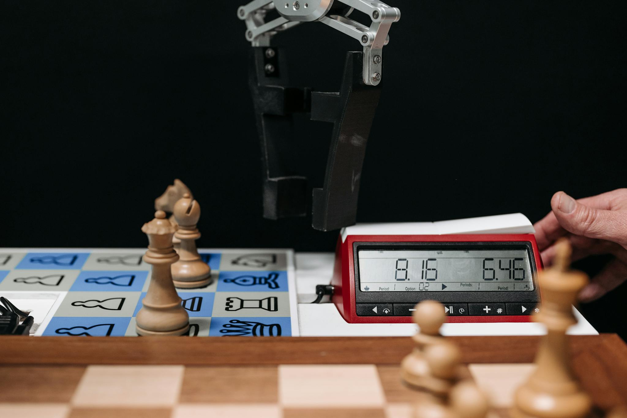 Robotic arm moves chess pieces on a board with electronic digital timer displayed.