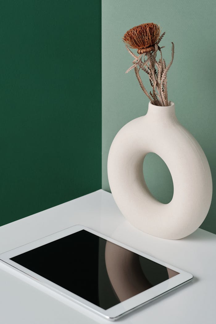 Elegant still life with a modern tablet and round ceramic vase on a two-toned background.