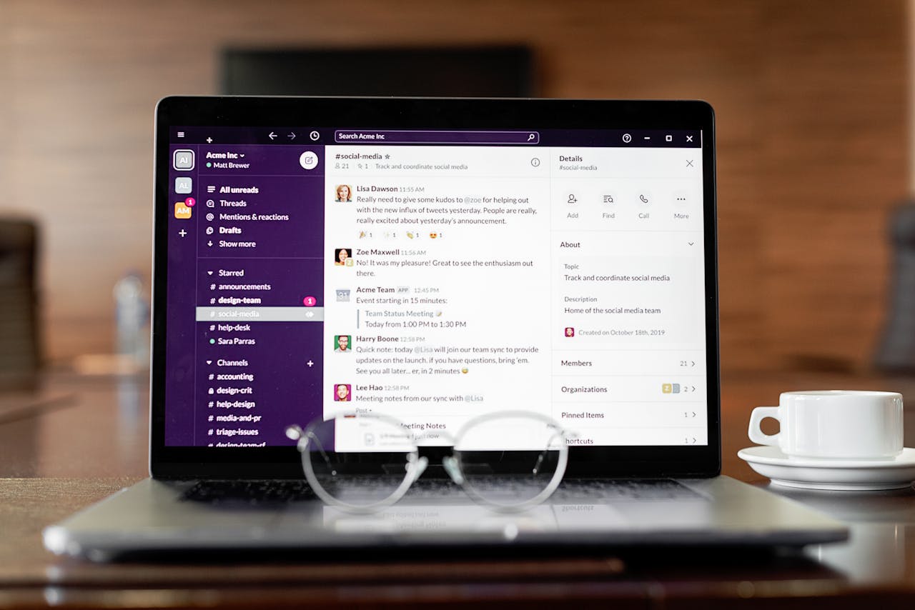 Laptop displaying a messaging app, with eyeglasses and coffee cup on a wooden table.